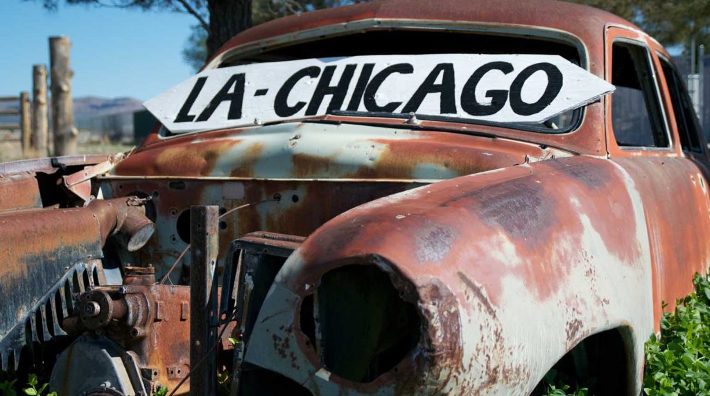 rusted-out vintage vehicle features a prominent wooden sign reading "LA-CHICAGO"