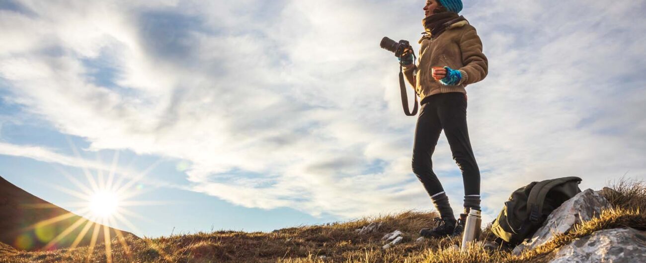 The image shows a person standing on a rocky hillside at sunrise The image shows a person standing on a rocky hillside at sunrise, Winter Sun Destinations