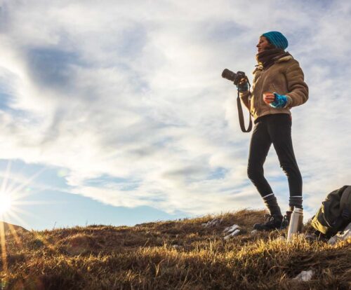 The image shows a person standing on a rocky hillside at sunrise, Winter Sun Destinations