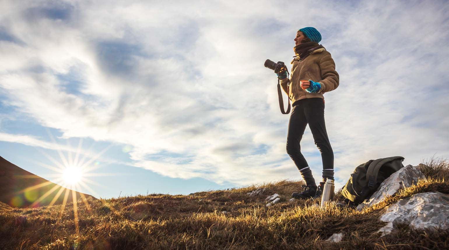 The image shows a person standing on a rocky hillside at sunrise, Winter Sun Destinations