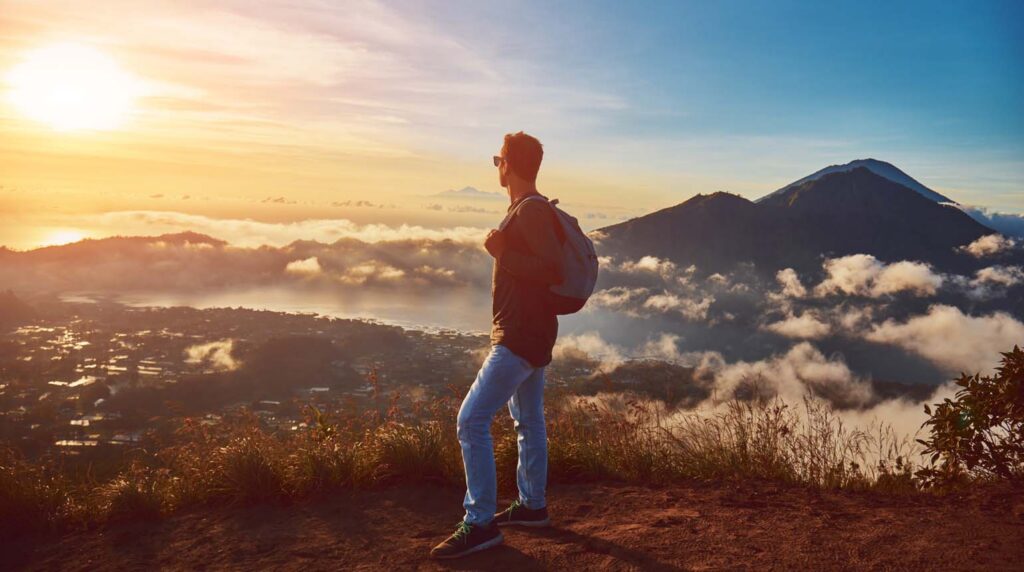 This image shows a hiker watching the sunrise from the summit of Mount Batur